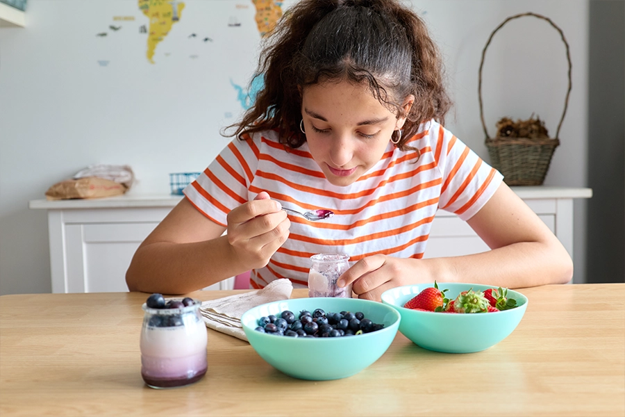 Teenage girl having a healthy breakfast with yogurt and fresh berries,